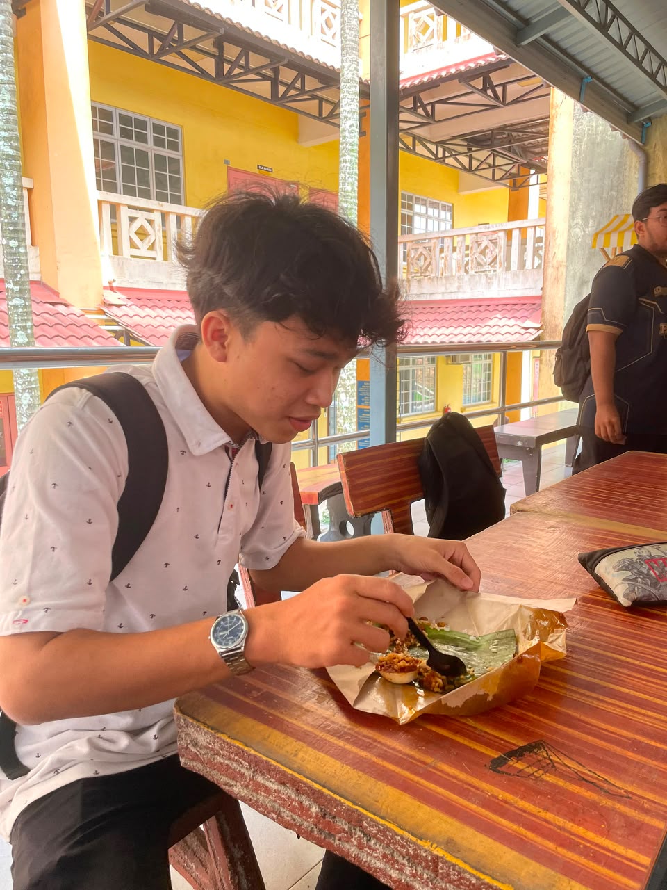Cook ladles reddish sauce onto rice and accompaniments served on a banana leaf in a busy kitchen.